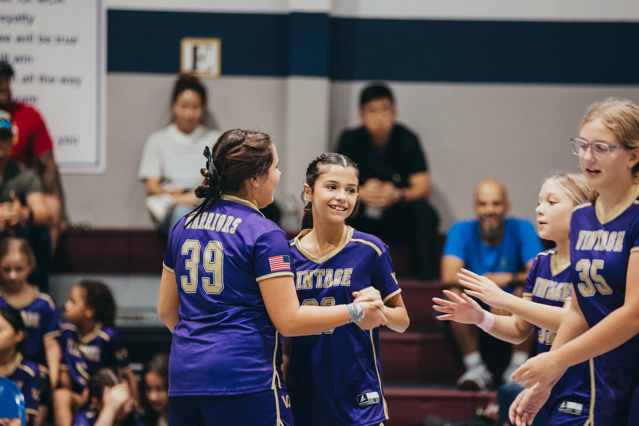 Two Vintage Warriors volleyball players celebrate on the court as teammates cheer.