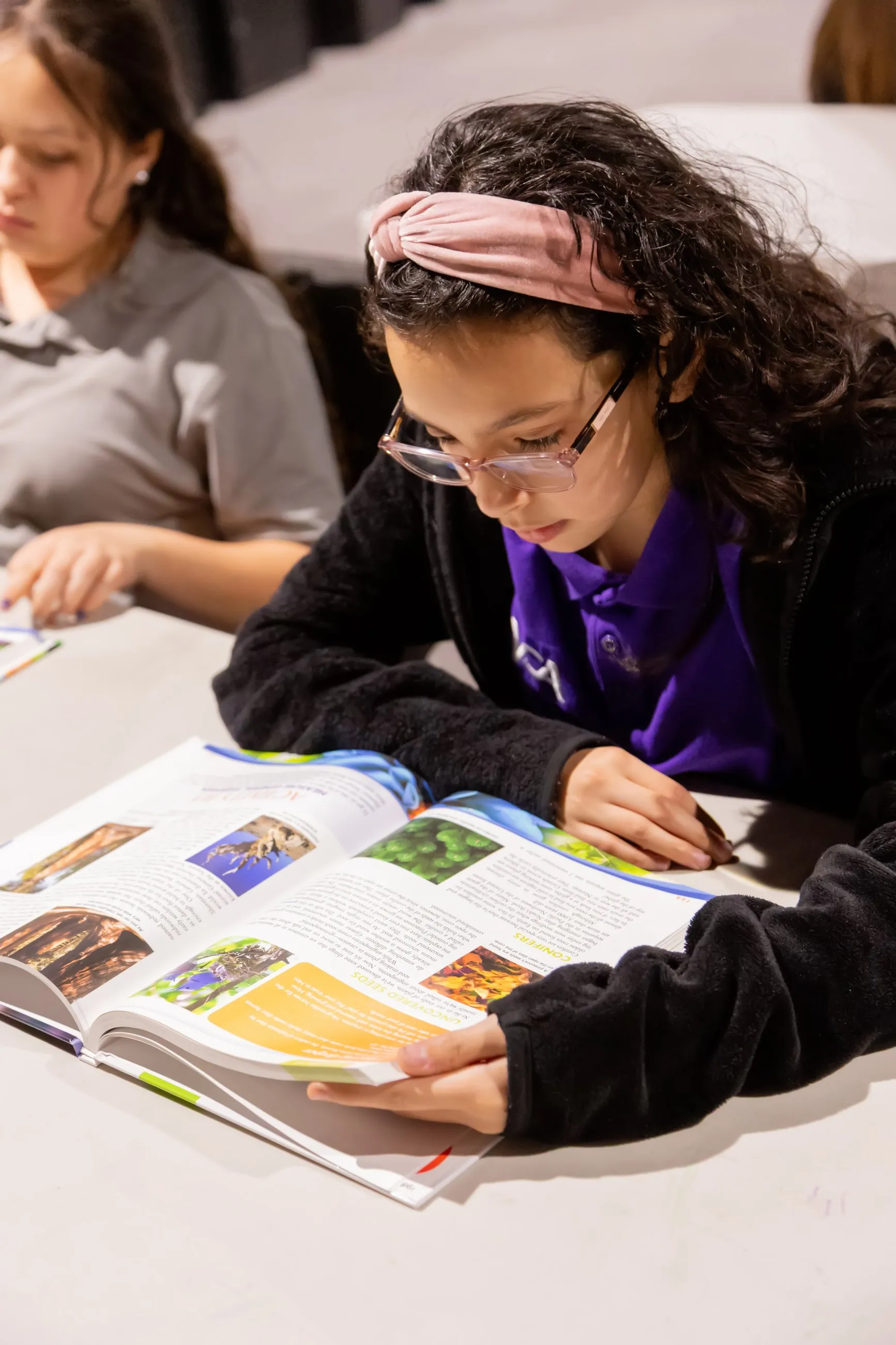 A student reads closely from an illustrated nature reference book at her desk.