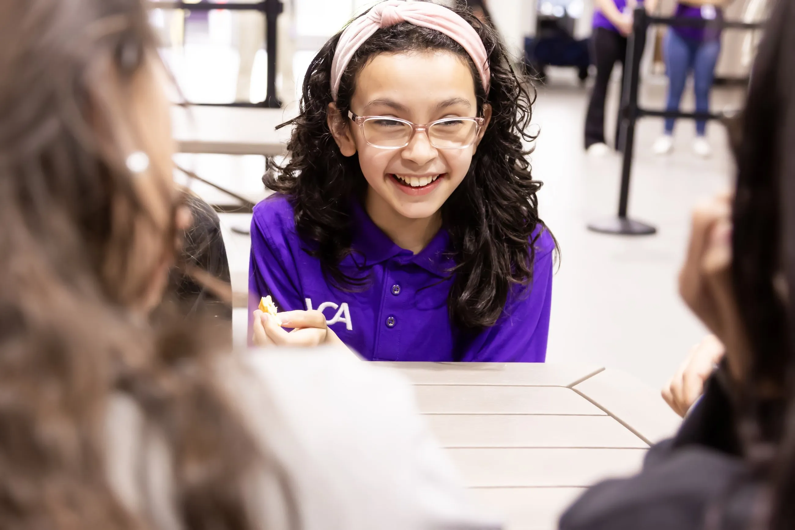 A smiling Vintage Christian Academy student at a lunch table with classmates.